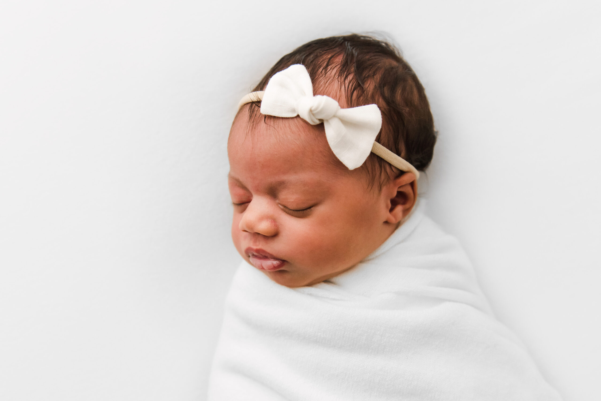 newborn baby on white blanket wearing simple white bow