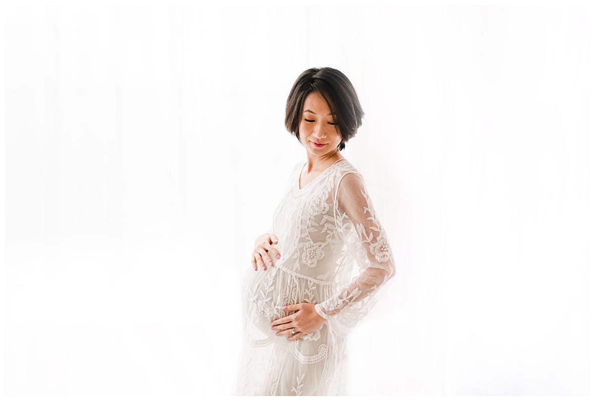 maternity picture in white lace dress in front of white curtain